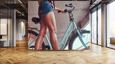 Close-up image of smooth slim female legs in blue sneakers near the city bike Wall mural