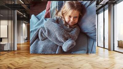 Close-up portrait of a little girl in warm sweater lying on bed. Wall mural