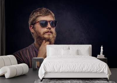 Close-up portrait of a pensive bearded redhead guy wearing sunglasses dressed in an old-fashioned shirt on a dark background. Wall mural