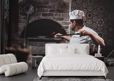 Experienced chef is putting his pizza to the oven using special giant spatula. Wall mural