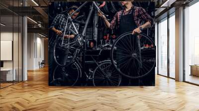 Good teamwork of two nice mans at busy bicycle workshop. Mans are wearing checkered shirts. Wall mural