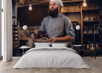 handsome bearded chef in uniform showing tray of fresh bread in the kitchen of bakery. Wall mural