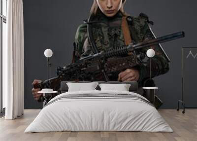 Portrait of a female soldier in military attire, holding a homemade automatic rifle, depicting a rebel or partisan in a Middle Eastern conflict against a gray background Wall mural