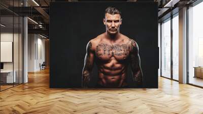 Portrait of a tattooed muscular shirtless man with stylish hair posing at the camera on a dark background. Wall mural