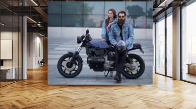 Portrait of attractive couple in denim jackets with motorbike near big glass building at city centre. Wall mural