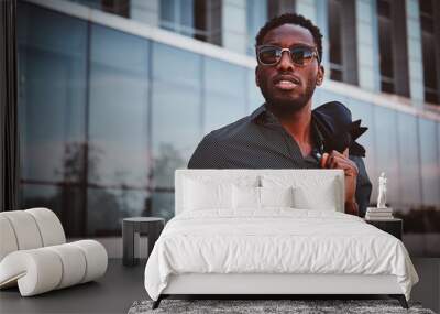 Portrait of pensive modern afro man with sunglasses and mobile phone over glass building background. Wall mural