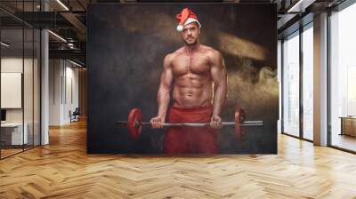 Portrait of shirtless man in Santa costume with barbell in hands. Wall mural