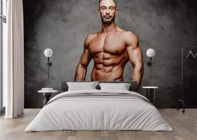 Shirtless adult male bodybuilder posing for a photoshoot shirtless in a dark studio Wall mural