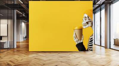 Skeleton sipping coffee wearing a yellow beanie hat. Wall mural