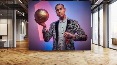 Stylish and succesful football trainer dressed in custom suit with jewellery poses with golden ball in abstract light background. Wall mural