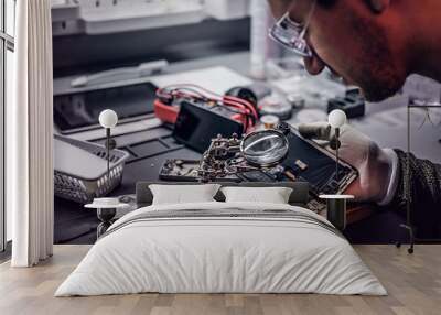 The technician uses a magnifying glass to carefully inspect the internal parts of the smartphone in a modern repair shop Wall mural