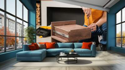 A man in an orange shirt is working on a piece of furniture. He is using a screwdriver to remove a drawer from a wooden cabinet Wall mural