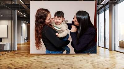 Two women are holding a baby. The baby is smiling and the women are smiling back. Scene is happy and joyful Wall mural