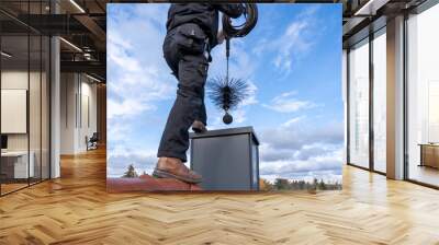 Chimney sweep cleaning a chimney standing on the house roof, lowering equipment down the flue Wall mural