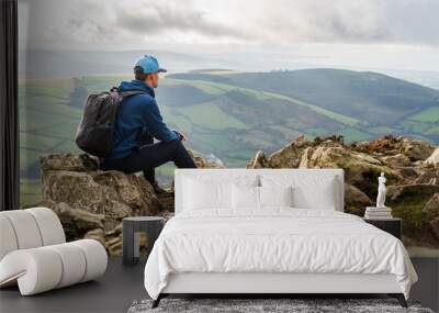 Hiker enjoying the view from the top of the Great Sugar Loaf Mountain in Ireland on a wet and cold winter day, while resting on the rugged rocks after a strenuous hike. Wall mural