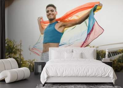 Young gay man wearing make up holding lgbt rainbow flag outdoors - Focus on face Wall mural