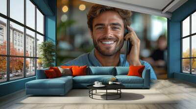 A happy young businessman is talking on the phone while standing in an office, wearing a blue shirt Wall mural