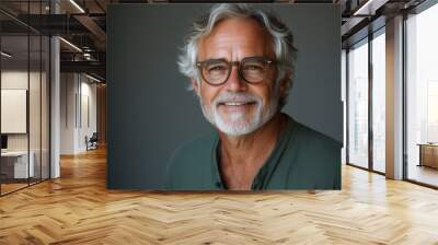 A senior man in his late fifties, smiling and wearing glasses against a white background. He is dressed casually with short grey hair and brown eyes Wall mural