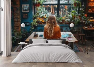 A woman sits at a desk in a room with plants and a window Wall mural