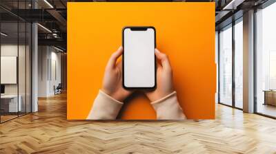 Hands Holding a Smartphone with a White Screen on Orange Background Wall mural