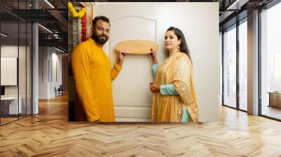 Happy indian couple of standing in their new house with name plate in hand. concept of new festival purchase. Wall mural