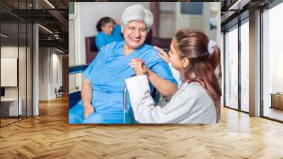 Happy indian elderly female patient looking at doctor in hospital ward while sitting on wheel chair, Old people healthcare concept. Wall mural