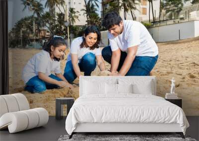 Happy indian family of three making sand castle or home at the beach enjoying holiday, Young parents with daughter playing outdoor, vacation. Wall mural