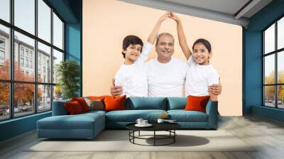 Happy indian senior man with kids wearing white casual t-shirt make home pose with hand over isolated beige background. Wall mural