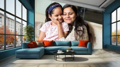 Happy playful indian mother hug her daughter sitting together at home, love and care, Asian woman with girl child playful. Wall mural