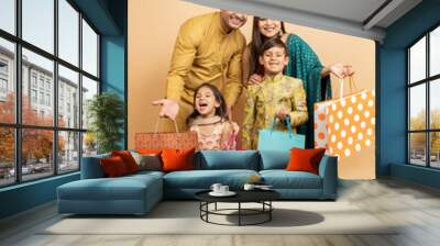 Happy young indian family wearing traditional cloths holding shopping bags and celebration diwali festival together isolated on beige studio background. Parents with kids celebrate festive season sale Wall mural