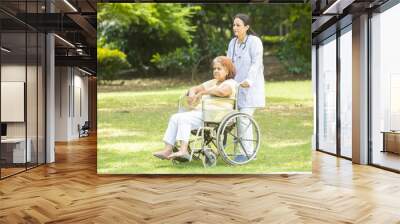 Indian caregiver nurse taking care of senior female patient in a wheelchair outdoor at park, Asian doctor help and support elderly mature older people. rehabilitation and health care. Wall mural