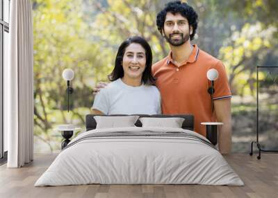 Portrait of happy indian couple standing outdoors in the park, Smiling urban city man and woman wearing casual t-shirt, looking at camera. husband wife. Wall mural