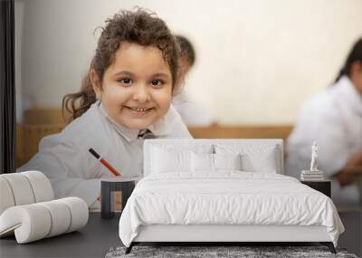 Portrait of happy indian schoolgirl sitting at desk in classroom, school kids with pens and notebooks writing test Elementary school, Education concept. Wall mural