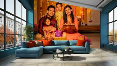 Portrait of happy young Indian family in traditional dress with lots of gifts around sitting on floor celebrating diwali festival at home. Wall mural