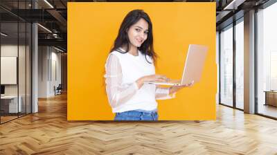 Portrait of happy young indian girl wearing white T-shirt using laptop isolated over orange yellow background. Studio Shot, Copy space, Asian woman using computer. Technology concept. Wall mural