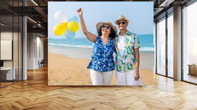 Senior indian couple with colorful balloon in hands walking together at the beach. Enjoying vacation, holiday at beach. Copy space. Retirement life. Wall mural