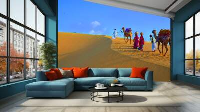 Two cameleers and women with camels walking on sand dunes of thar desert against blue sky , Jaisalmer, Rajasthan, India Wall mural