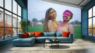 Two Cheerful young indian women friends covered with colorful powder or gulal celebrating holi festival of colors. Culture of india.Girls laughing having fun together. Wall mural