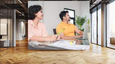 Two young indian business people sitting around a table during office meeting listening to the presentation. Start up, people and workplace concept. Wall mural