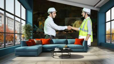 Two young male and female indian engineers wearing safety hard hat and vest do handshake at industrial factory. Wall mural