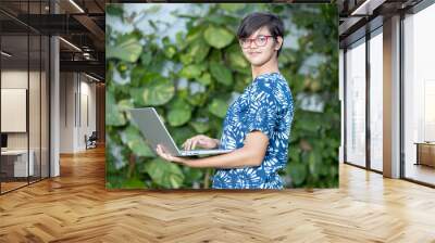 Young beautiful Indian teenager girl working on a laptop wearing casual t-shirt and spectacles, Asian adult female using computer. cloud computing and it professional, web development. Wall mural