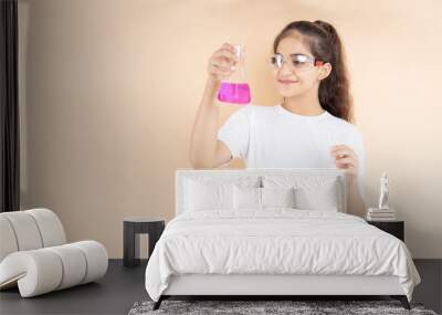 Young indian girl student doing science experiment holding colorful chemical flask isolated over beige background. Education concept. Wall mural