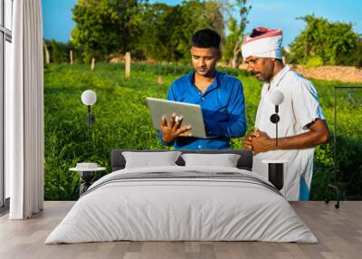 Young indian man agronomist holding laptop standing with farmer at agriculture field Wall mural