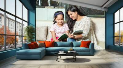 Young indian mother helping little daughter with study at home, Asian girl child with notebook doing homework with her mom.  Wall mural