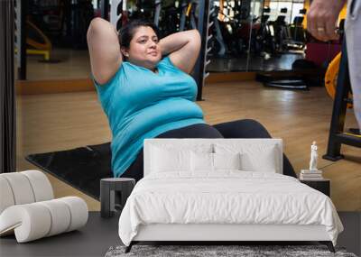 Young overweight indian woman lying doing crunches workout in gym to lose weight and burn belly fat exercise. fitness and health care Wall mural