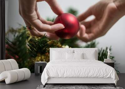 Female hand placing red holiday bauble on Christmas tree Wall mural