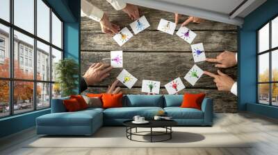 Teamwork and brainstorming concept with businessmen seated around a table each pointing to cards with colorful sketches of light bulbs conceptual of bright ideas and solutions arranged in a circle. Wall mural