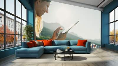 Young woman sitting on a beach at sunrise browsing on her digital tablet Wall mural