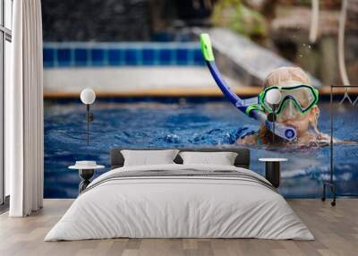 A four-year-old child swims actively in the pool of his house in a mask and snorkel. Wall mural