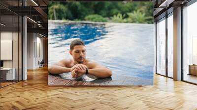 An attractive sporty man in an outdoor pool looks at the smartwatch tracker after an active swim. Wall mural